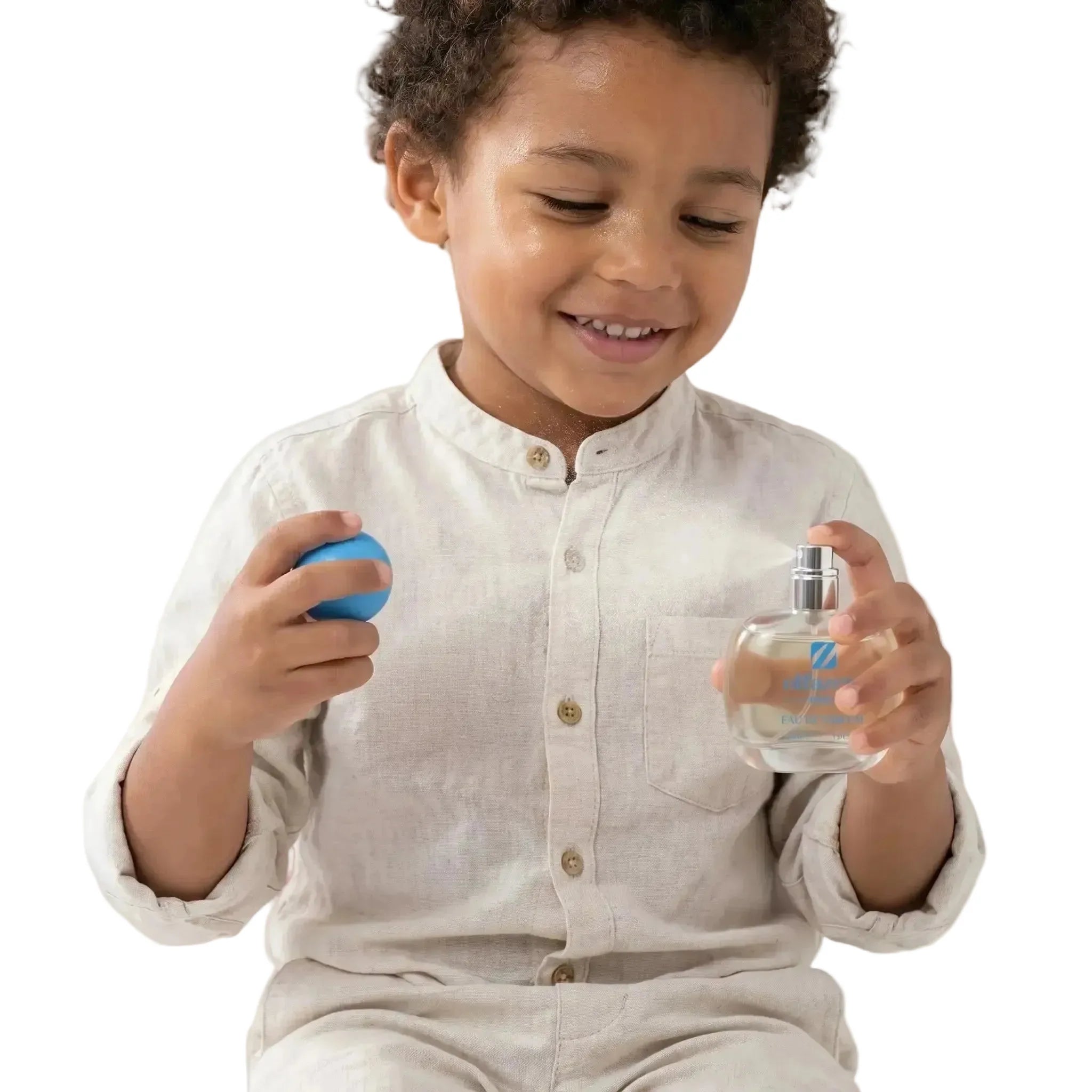 Petit garçon souriant qui vaporise un flacon d'eau de parfum pour enfant avec un bouchon bleu.