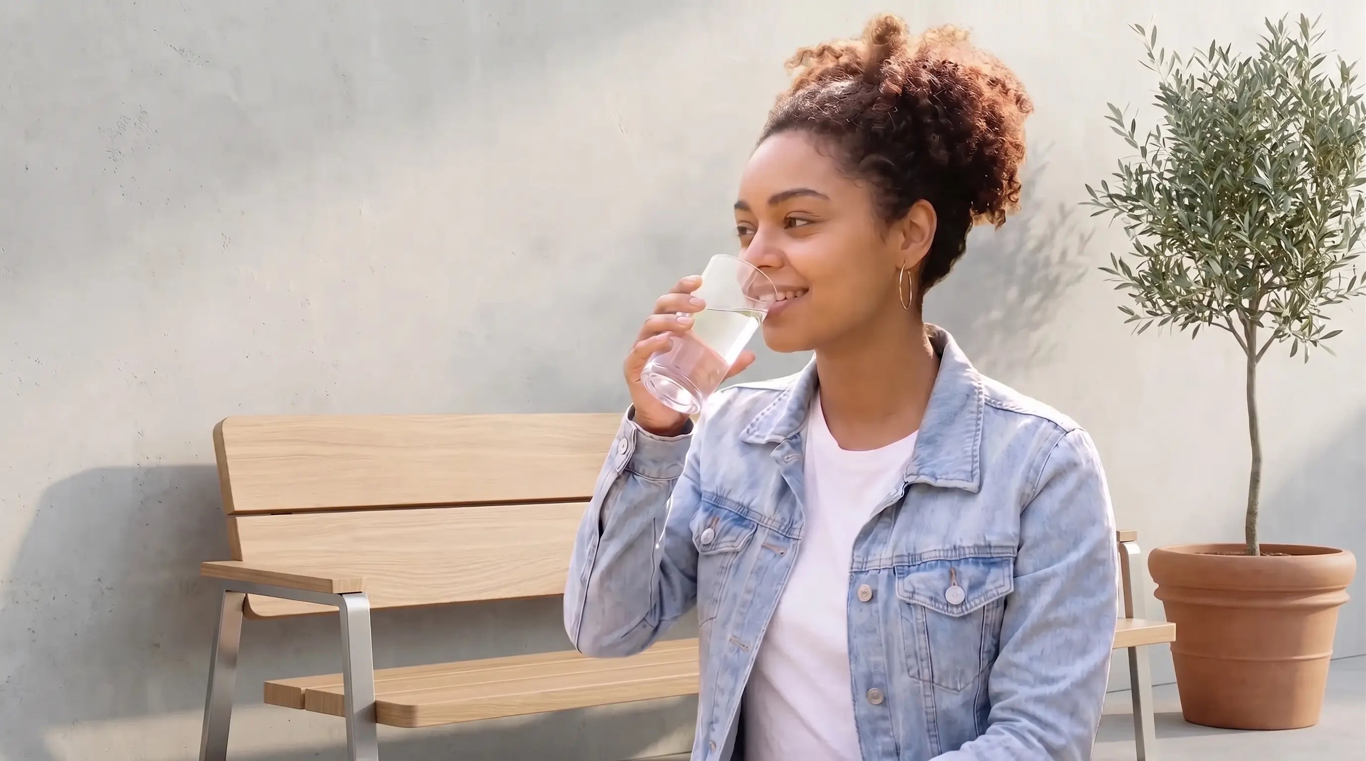 Femme souriante buvant un verre d'eau psur une terrasse ensoleillée.