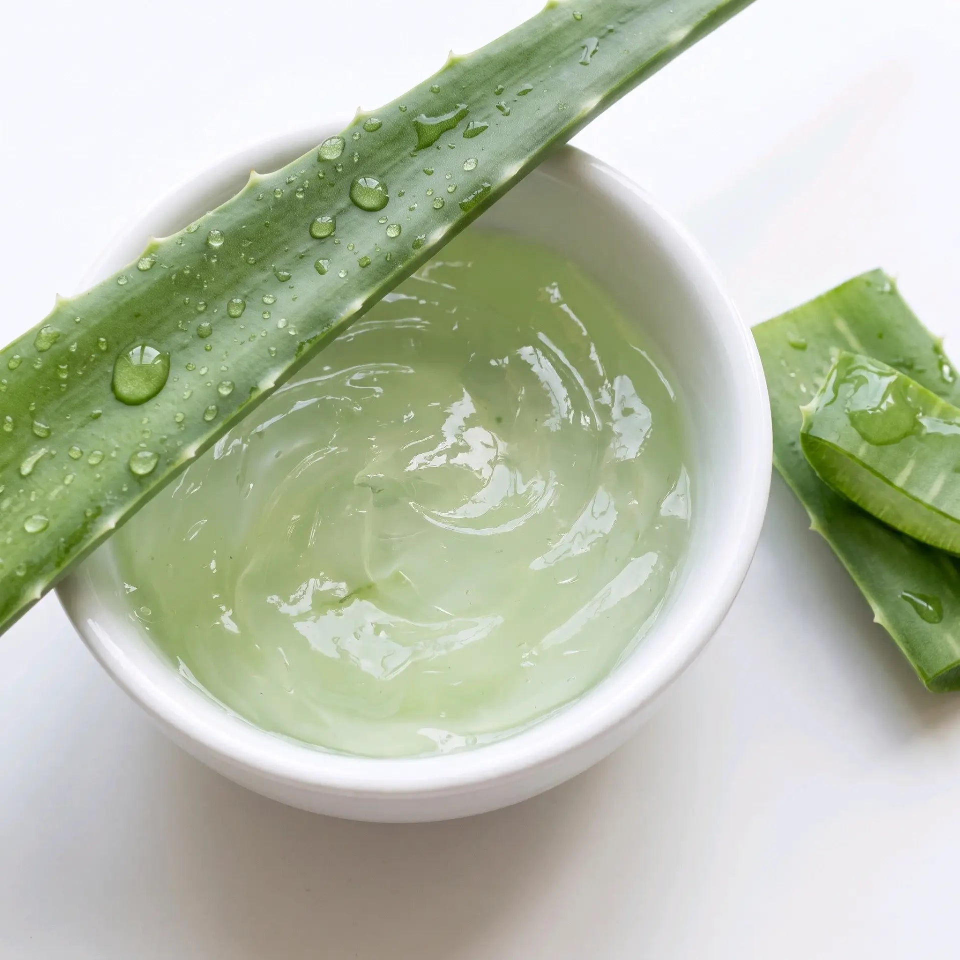 Bol blanc contenant du gel d'aloe vera pur et transparent, de feuilles fraîches d'aloe vera coupées posées de côté