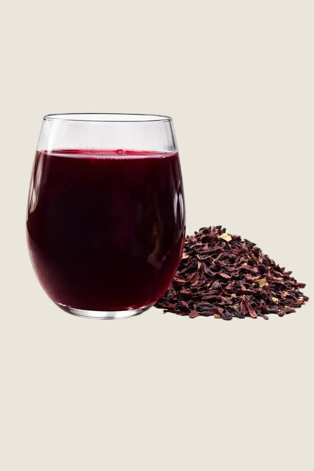 Un verre d'infusion de bissap rouge foncé à côté d'un tas de fleurs d'hibiscus séchées sur fond blanc